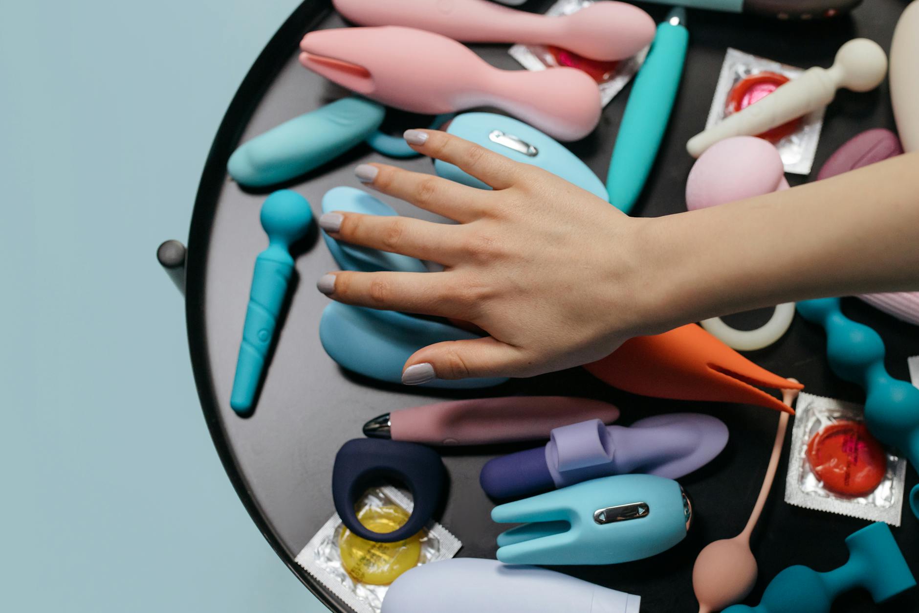 Hands selecting from a variety of colorful sex toys on a table, representing choice and accessibility