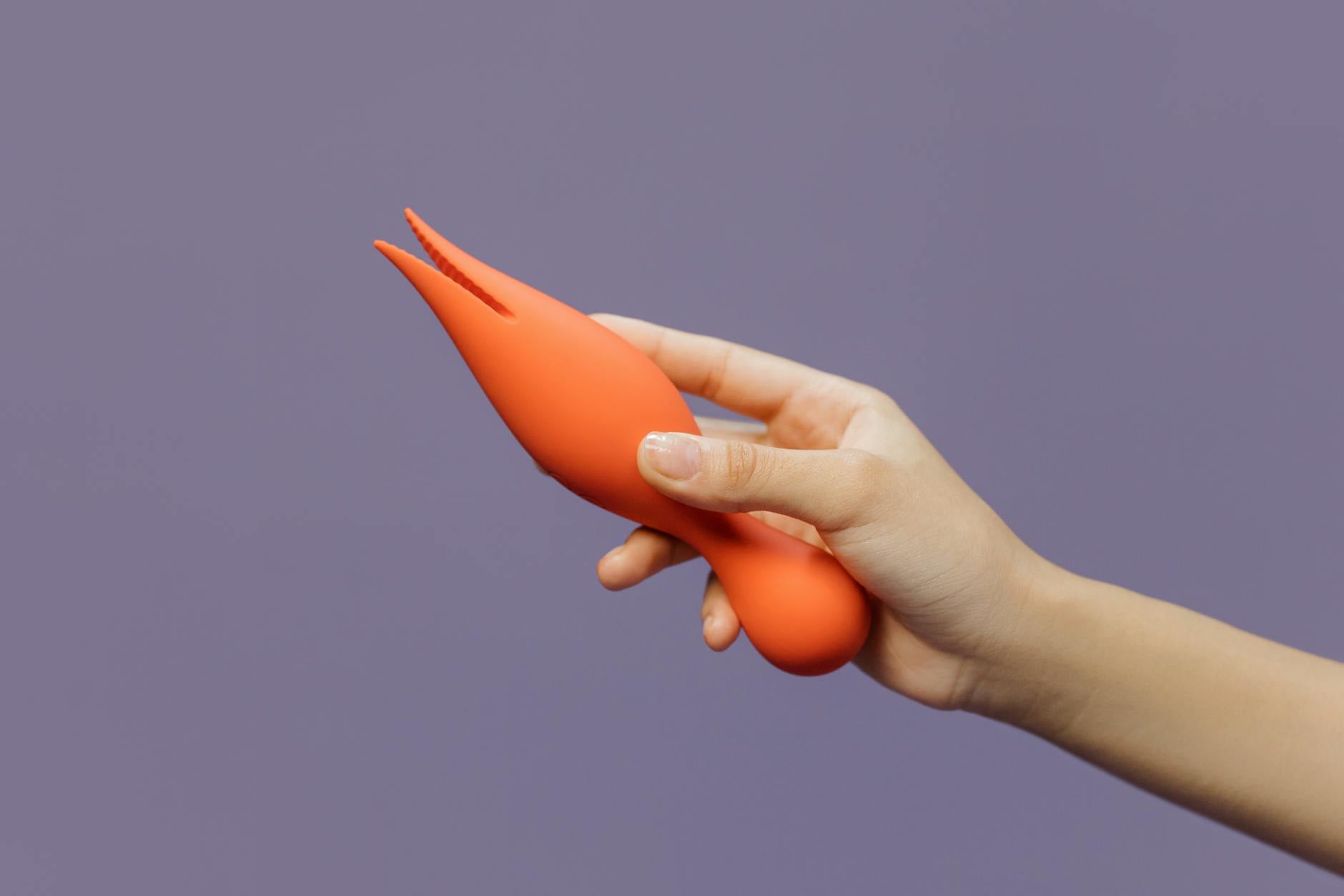 Hand holding a lemon-colored clitoral vibrator against a purple backdrop, showcasing design and color