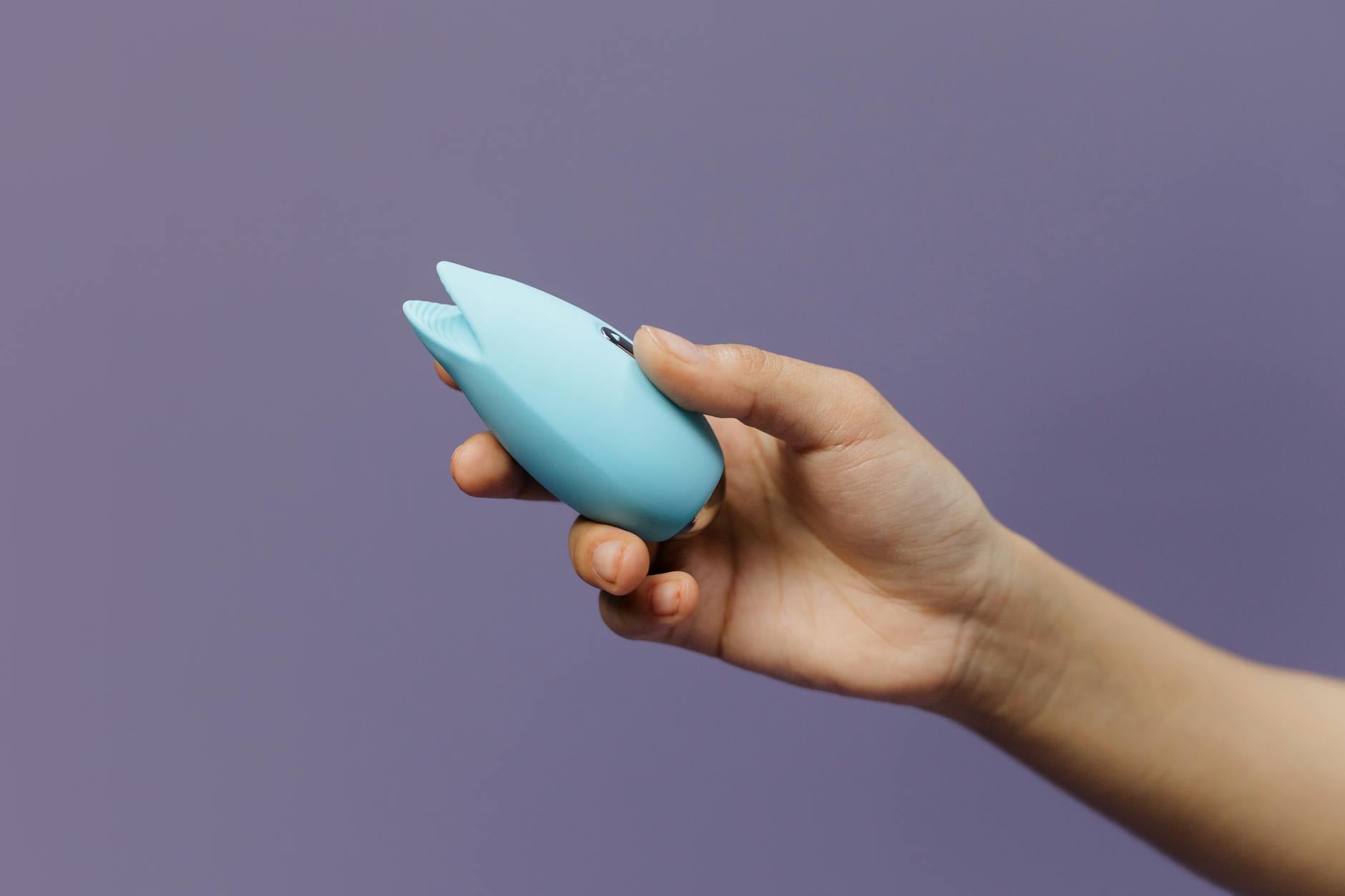 Close-up of hands holding a sleek blue vibrator against a purple background