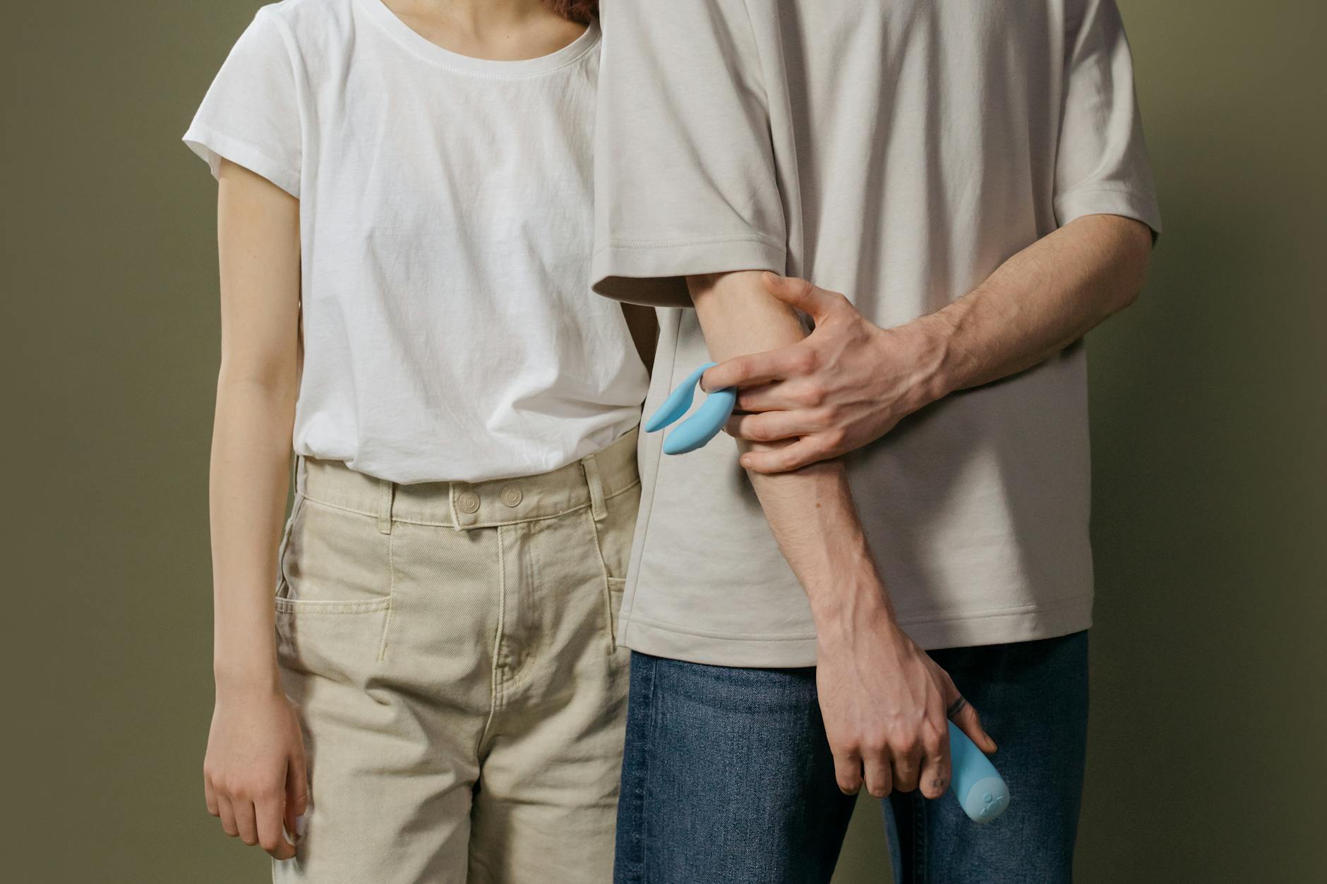 A young couple standing together holding a blue vibrator, representing modern intimacy and partnership