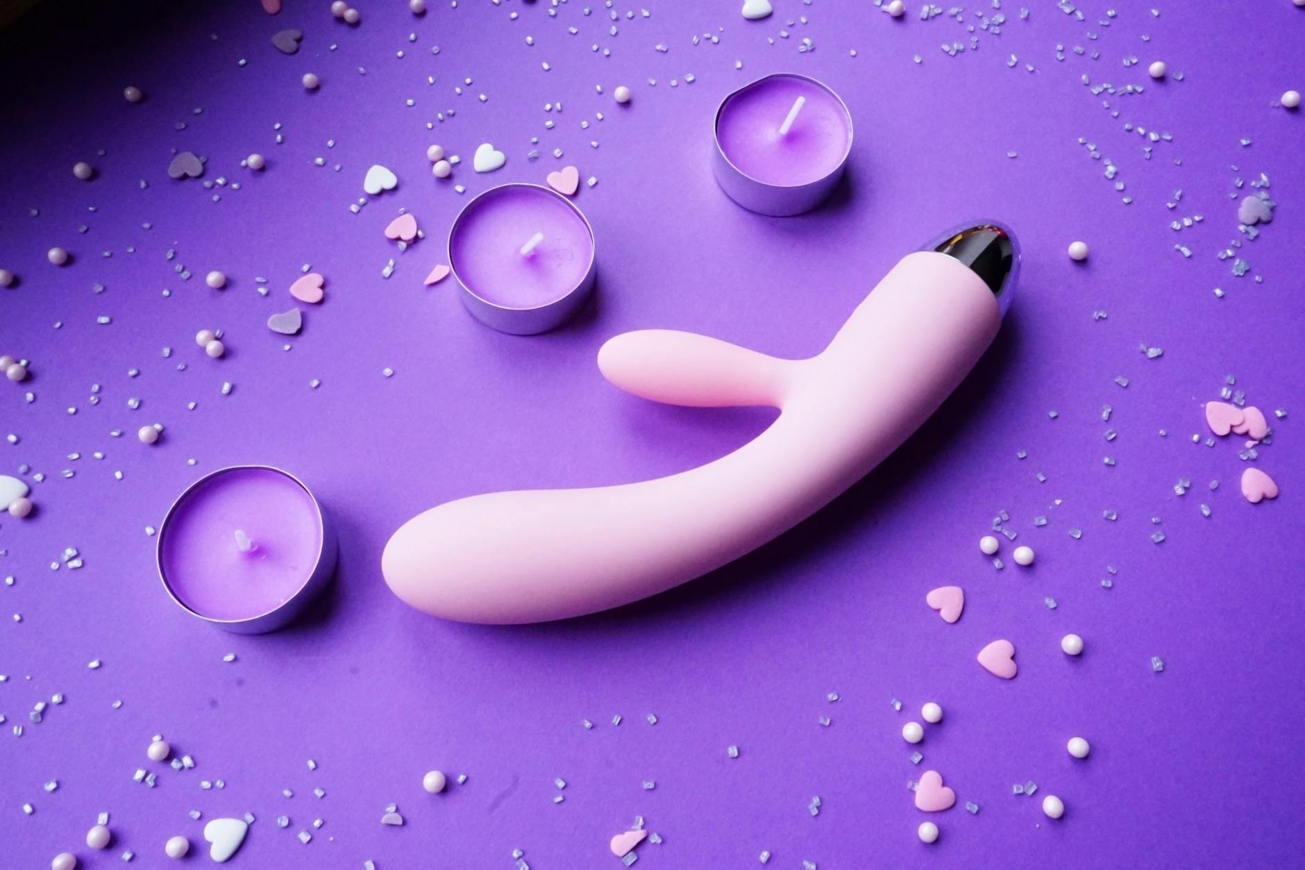 A blue silicone sex toy held in hand against a solid purple background