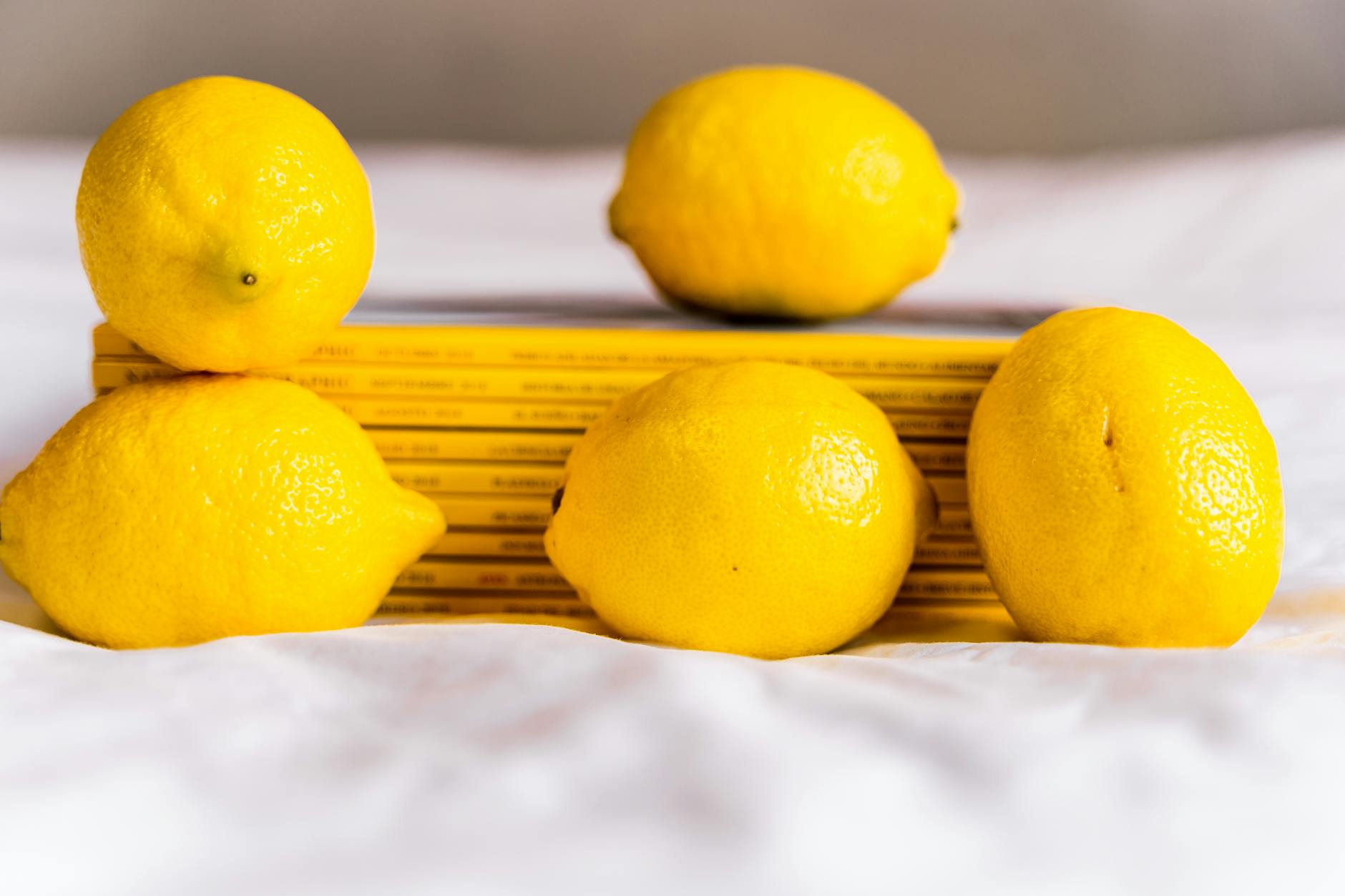 A yellow lemon-shaped vibrator on a soft yellow background surrounded by fresh lemons